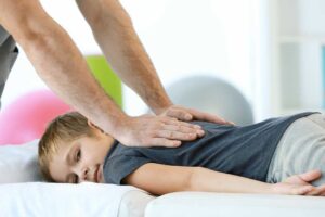 A chiropractor gently adjusts a patient’s upper back while the patient relaxes on a treatment table.